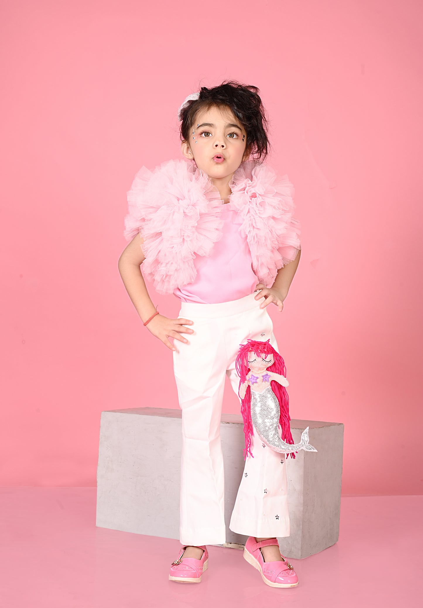 Child wearing a pink outfit with a feather boa against a pink background