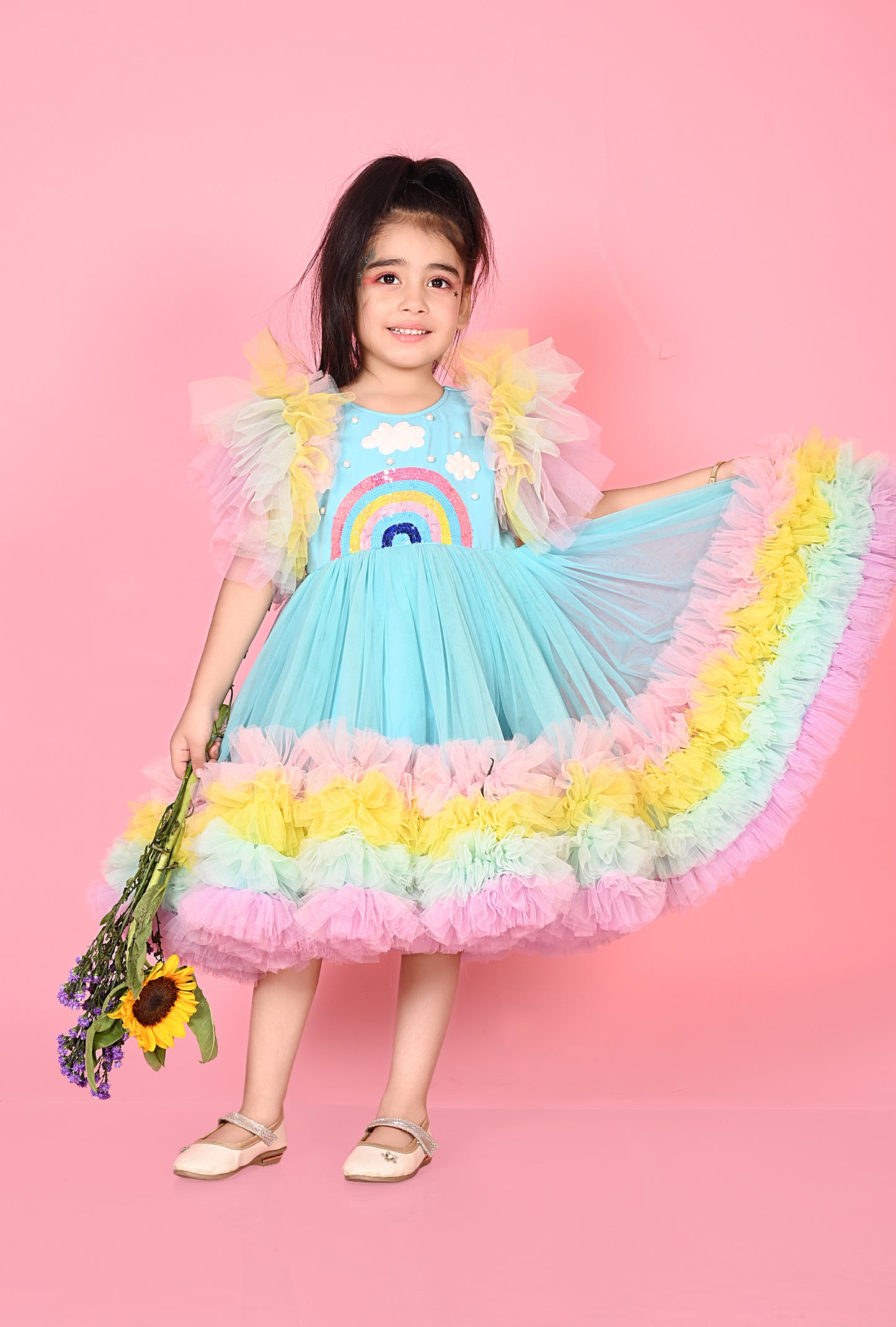 Young girl in a colorful dress with a rainbow design against a pink background